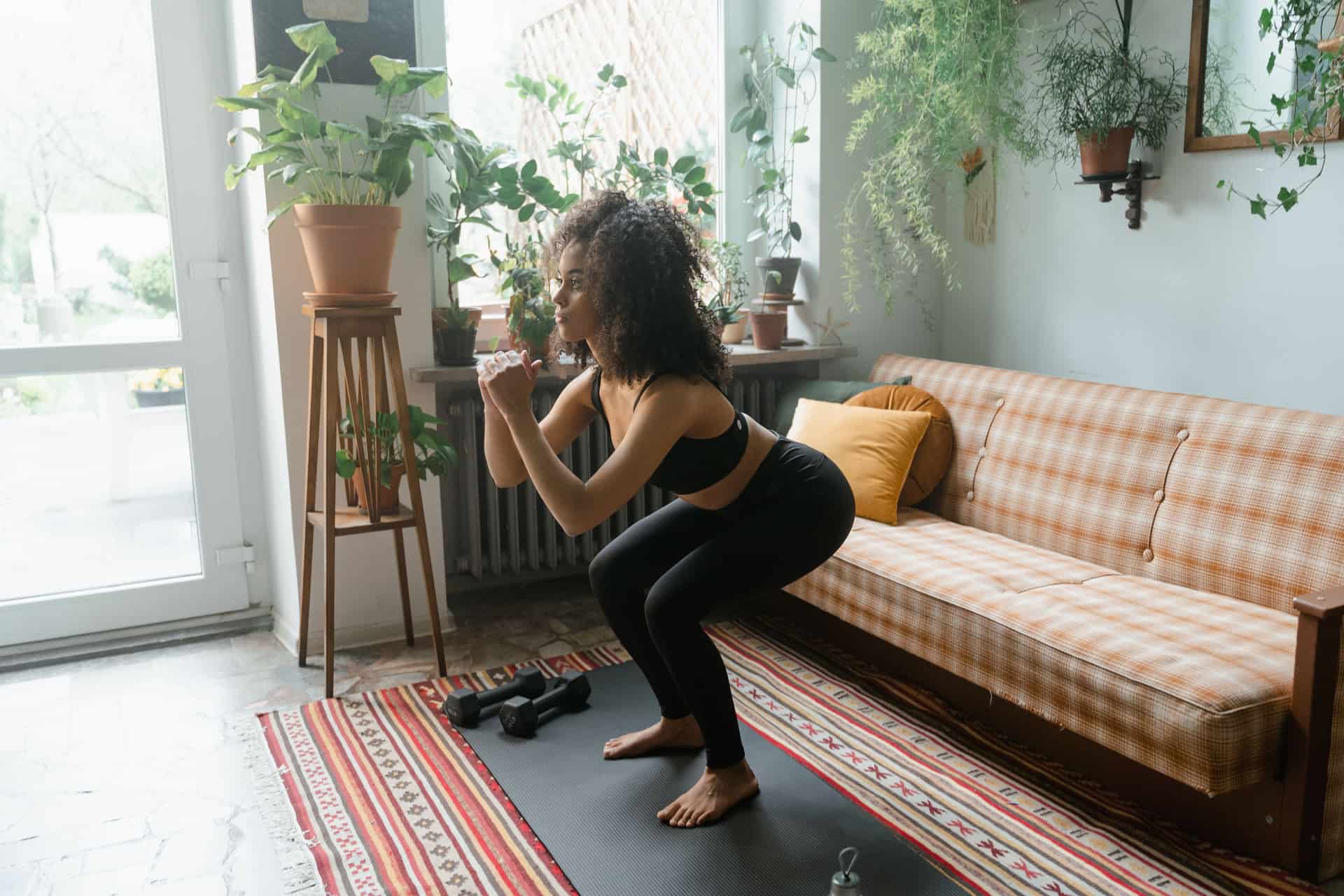 Woman performing a squat with dumbbells in a plant-filled living room